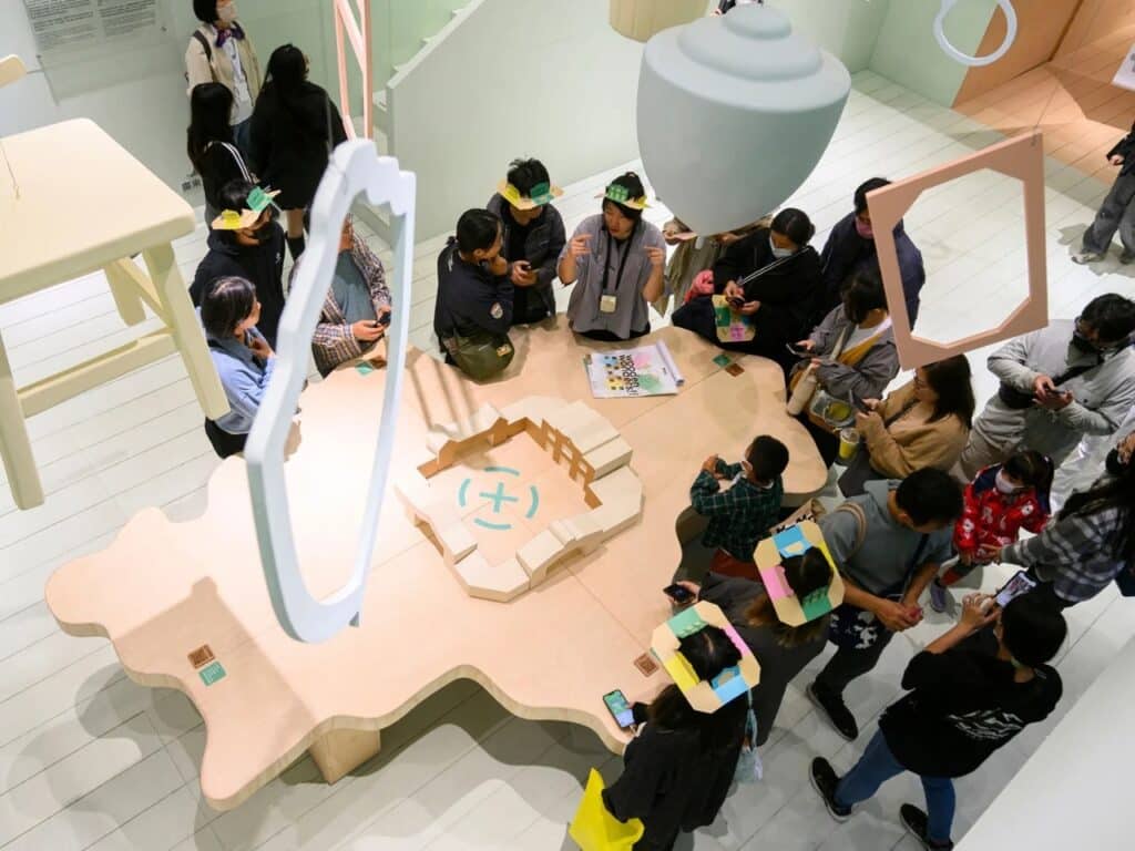 High angle view of a group of people wearing paper hats gathered around an interactive map table in the pavilion.