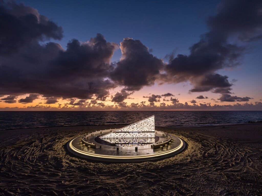 Dramatic wide shot of the Nahnu Library under a cloudy twilight sky, with the structure glowing intensely on the dark sand.