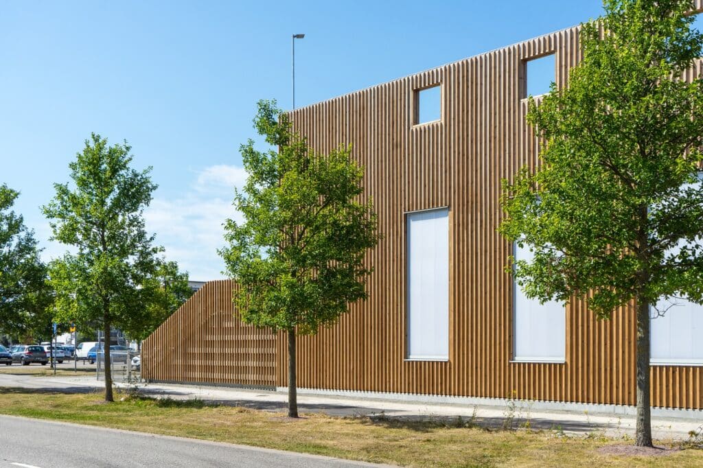 Close-up of the timber-slatted facade of &Auml;ngsdal School with integrated trees and street-side landscaping.