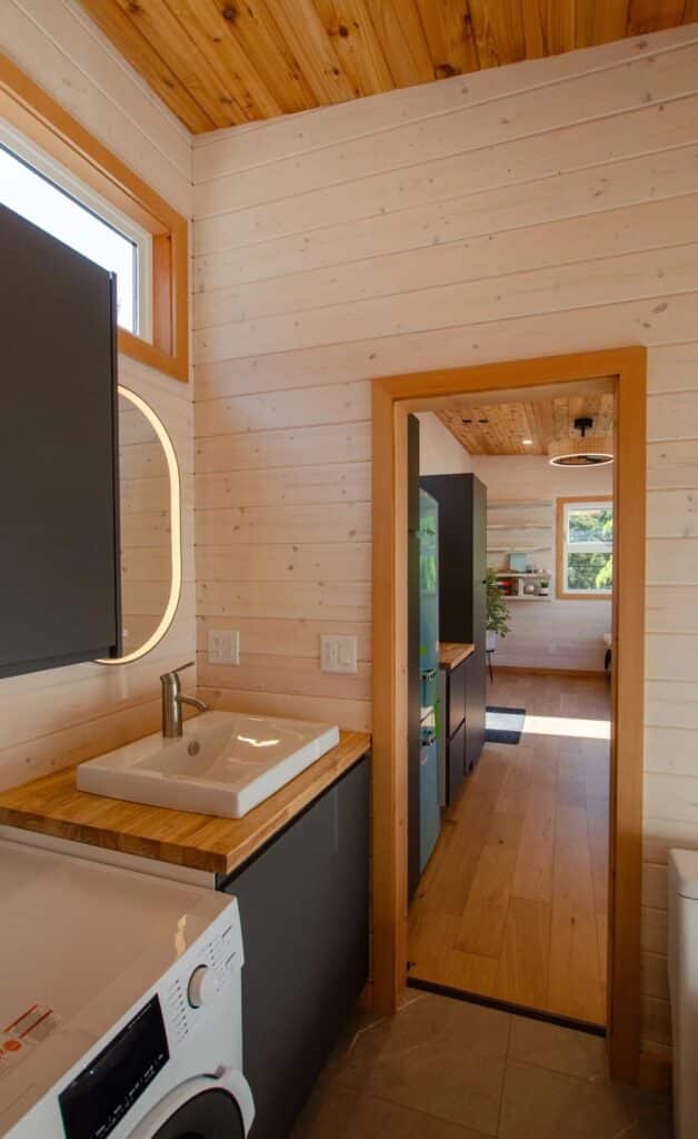 Modern bathroom sink with wooden countertop and an illuminated oval mirror in a tiny home interior.