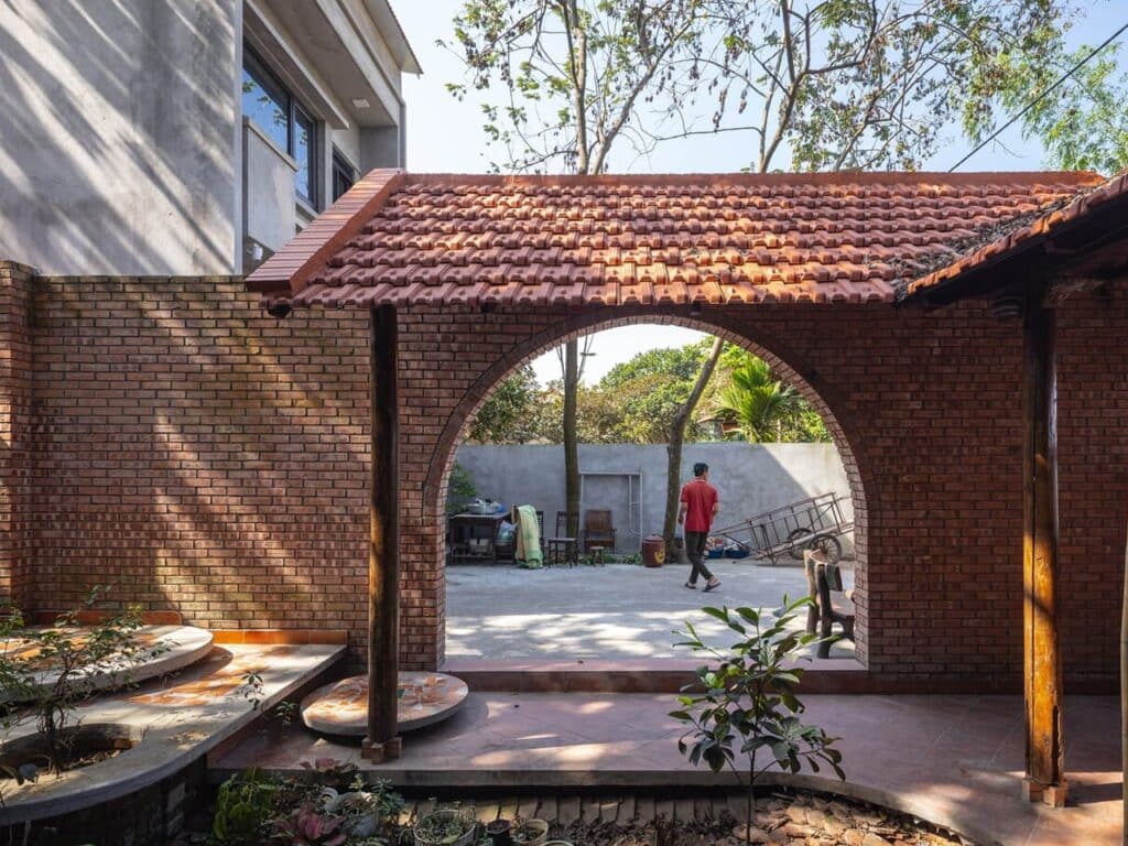 Nang House in Hanoi suburbs blending contemporary architecture with traditional elements, showcasing brick and wood materials, integrated gardens, and open spaces that connect family living with the natural environment.