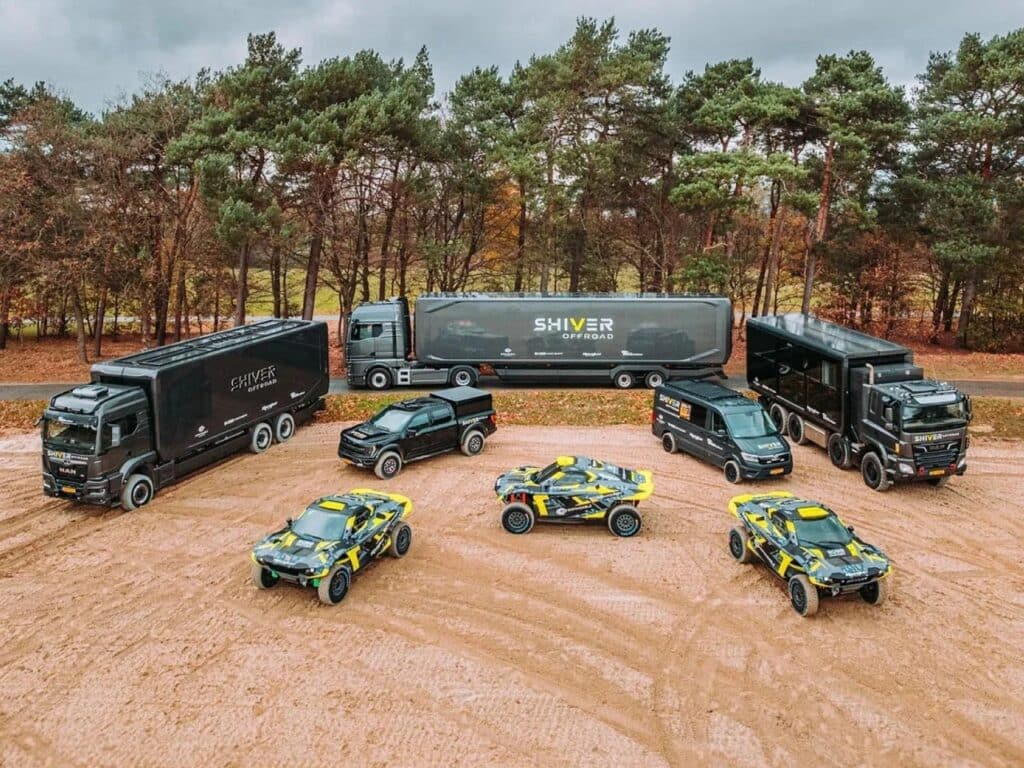 High-angle wide shot of the Shiver Offroad fleet in a sandy desert area, featuring multiple 6x6 motorhomes, support vans, and rally cars.