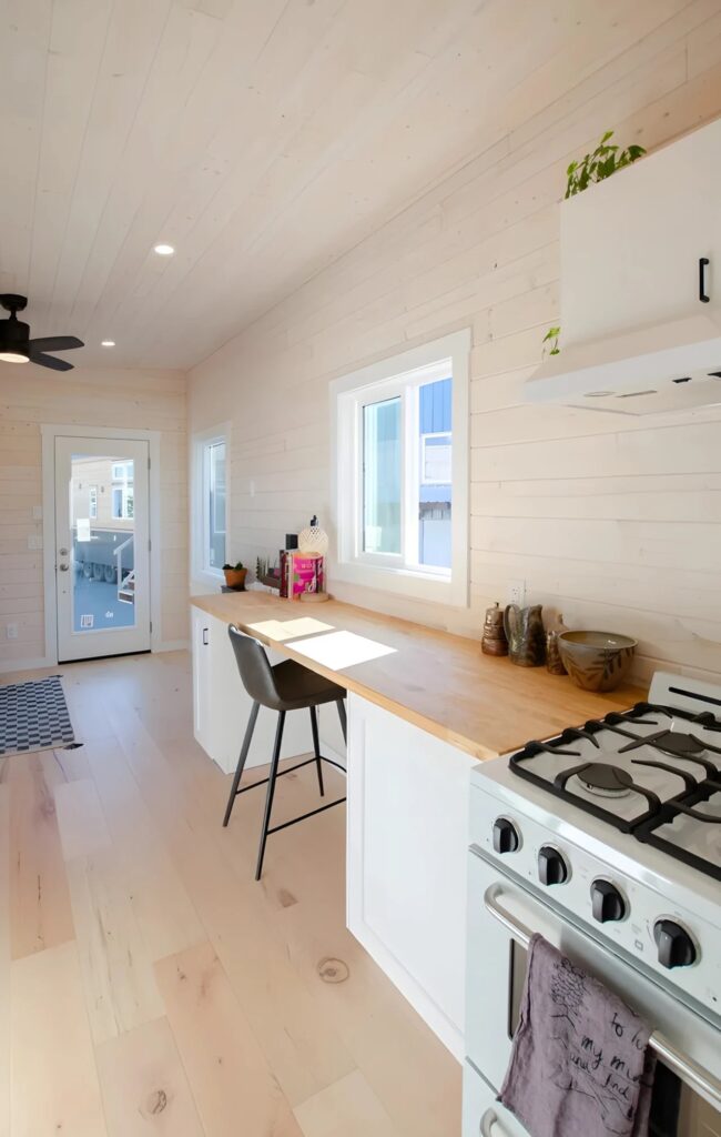 Linear kitchen layout in the Barred Owl tiny house featuring a white gas range, butcher block countertops, and a barn door.