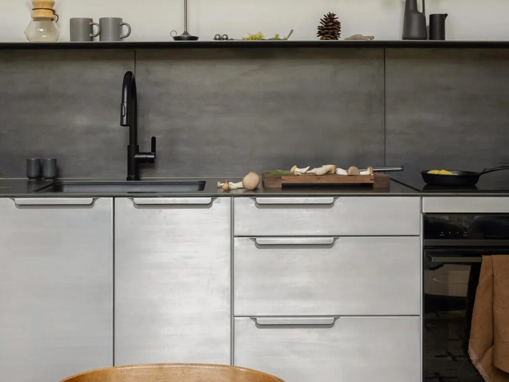 Close-up detail of the Wenatchee River Cabin kitchen, featuring matte gray cabinetry, a black faucet and sink, black backsplash, and a wooden cutting board with mushrooms.