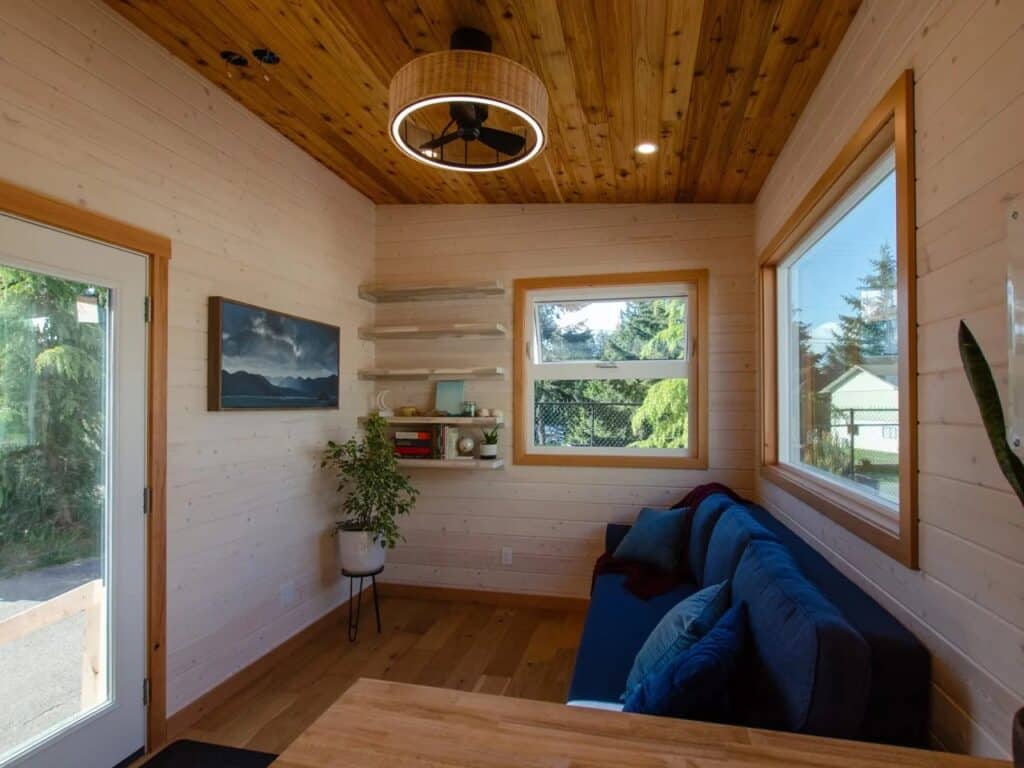 Full view of the Juniper living room showing floating shelves, a ceiling fan with light, and wall-mounted artwork.