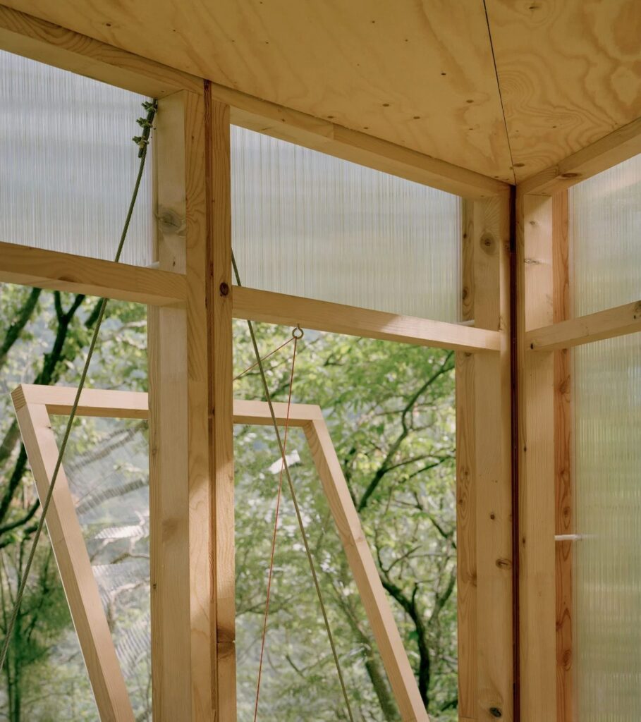 Detail of the timber framing and window mechanism of Casetta Tessino, showing the craftsmanship of the wooden joints and the forest view.