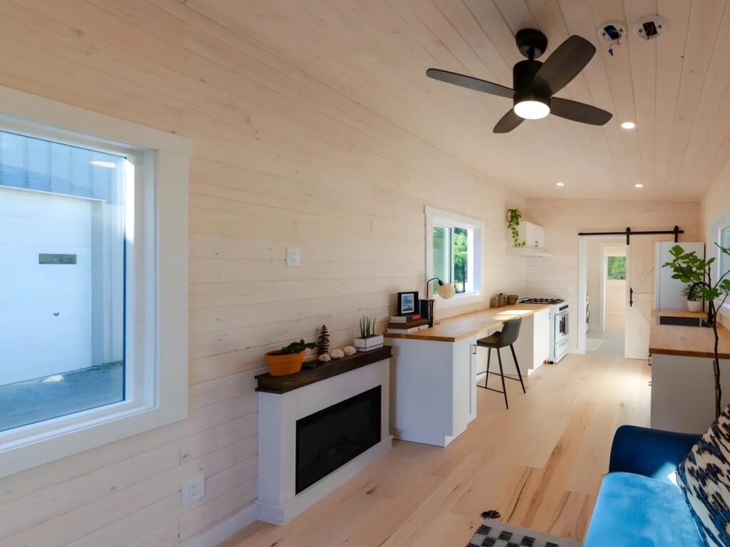 Long interior view of a tiny house showing the transition from living area to kitchen and bedroom.