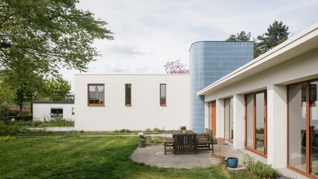 Outdoor terrace of a modern bungalow with wooden garden furniture, white walls, and a blue tiled tower.