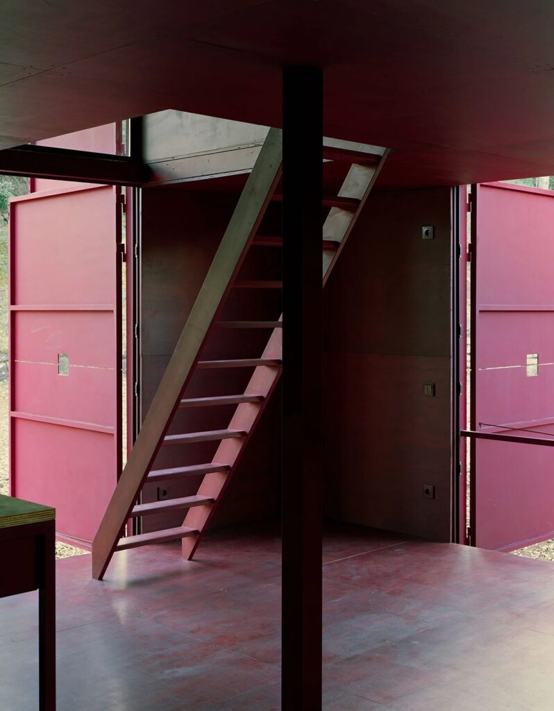 Close-up of the Prefab Changeover house with a section of its facade folded open to reveal a two-story glass window and interior view.