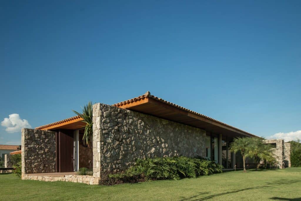 Exterior corner view of the Stone House showing the clay tile roof and the thick stone masonry walls in bright sunlight.