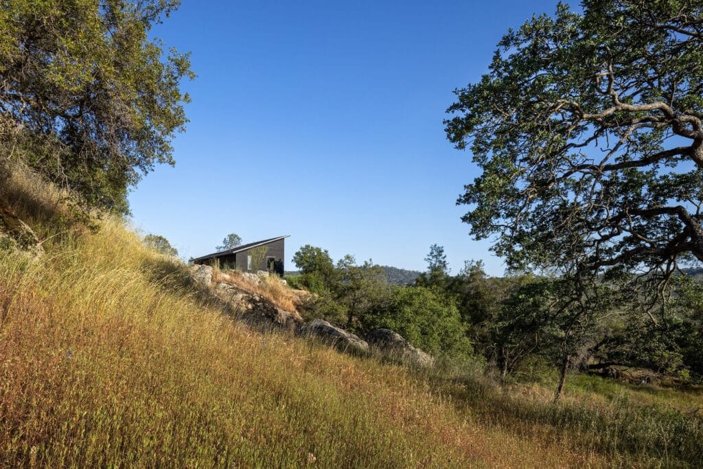 Side view of Casa Roca situated on a grassy hillside under a clear blue sky, showing its sloped roofline.