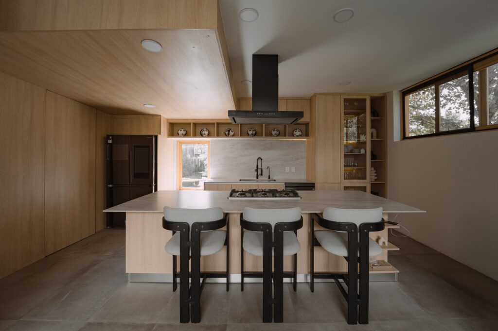 Casa EV residential design in Guadalajara featuring innovative integration of privacy, natural light, wooden materials, interconnected living spaces, central staircase, and landscaped exterior blending indoor and outdoor experiences.