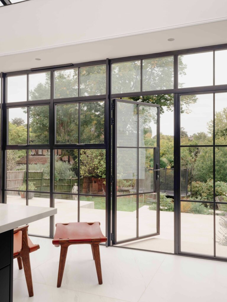 Detail of black-framed Crittall-style glass doors open to a sun-drenched terrace at Wimbledon House.