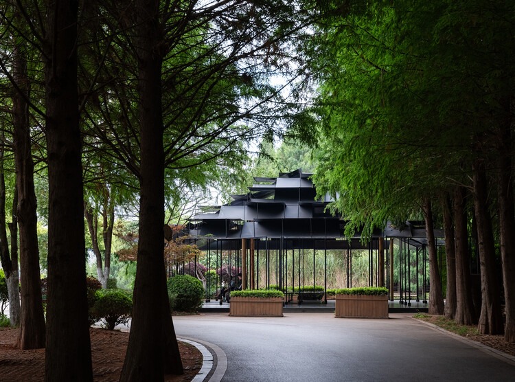 View of the black Laoyuting Pavilion nestled between tall, dense trees on a curved park road.