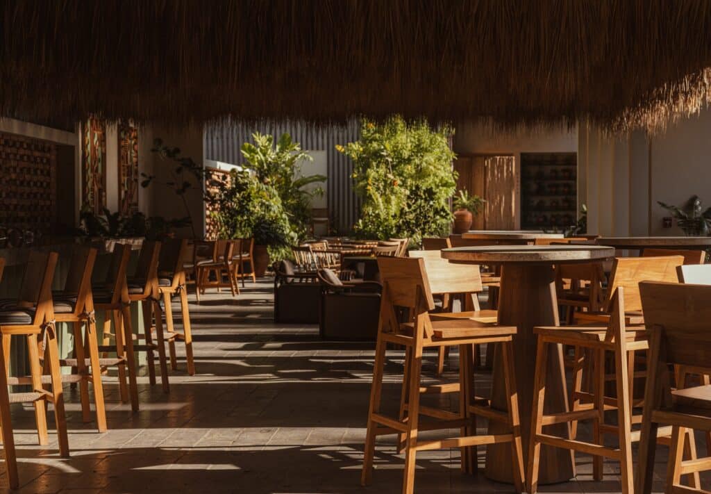 Interior seating area of the beach club with wooden furniture and a rustic thatched ceiling.