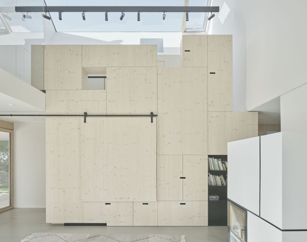 Custom-built light wood storage wall with integrated bookshelf and sliding panel in the minimalist interior of House Am Feuerbachl.