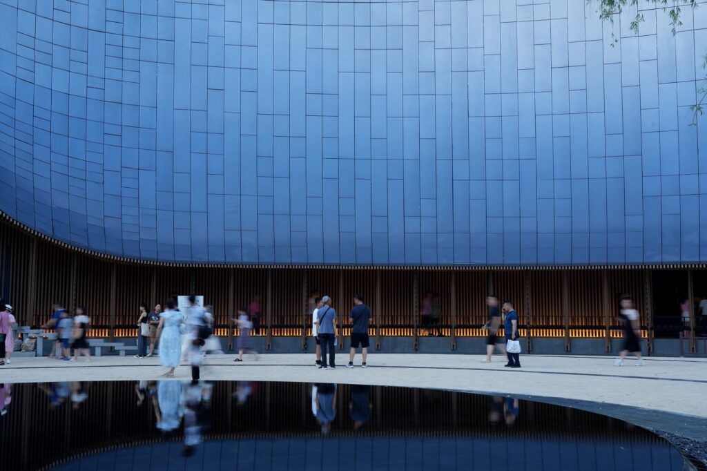 Close-up of the blue-tiled curved wall of Zhouzhuang theater with people walking in a blurred motion at the base.