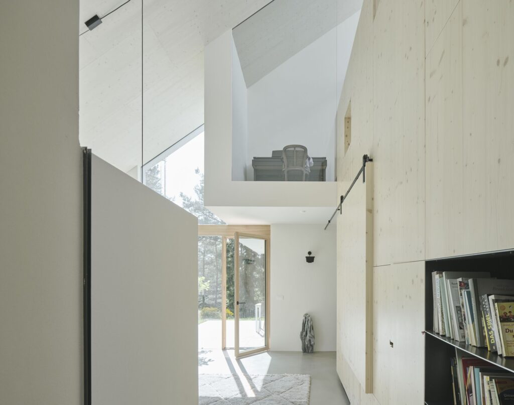 Interior view looking toward a glass door and an upper mezzanine level with a piano in House Am Feuerbachl.