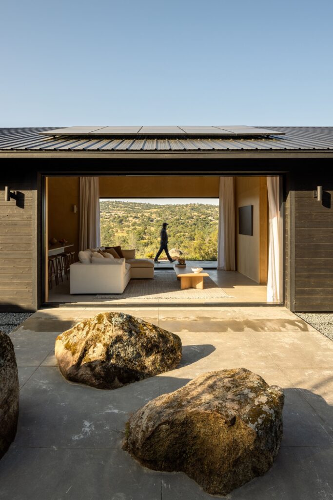 A wide-angle view from the exterior patio looking through the transparent living room of Casa Roca toward the mountain valley.