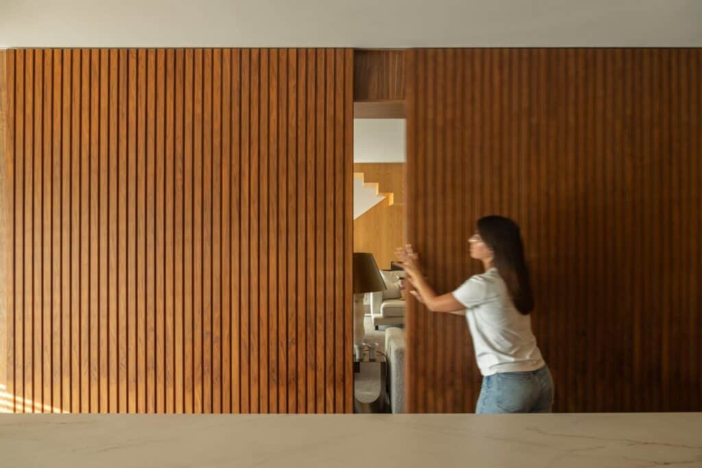 Person sliding a large vertical wooden slat door inside Casa do Engenho to reveal the living area.