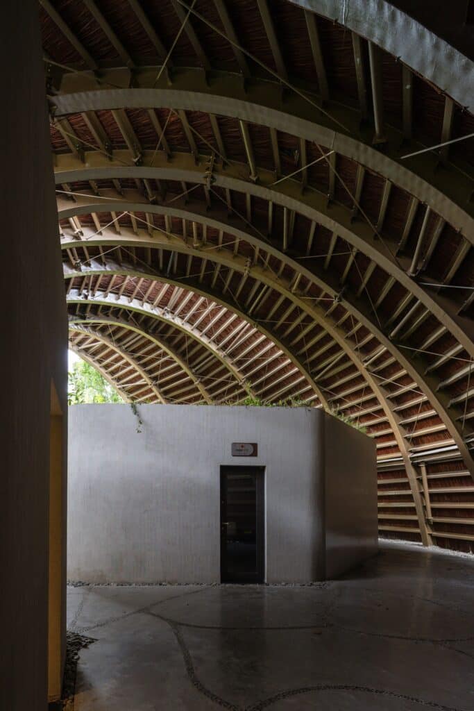 Looking up at the rhythmic arched ceiling structure of Goot Garden House made of layered materials and steel supports.