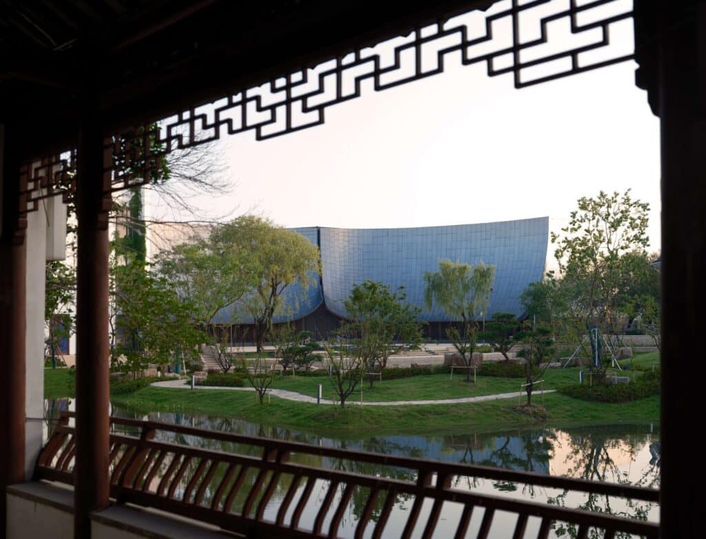 View of the Zhouzhuang theatre's blue curved facade framed through a traditional Chinese wooden window lattice.