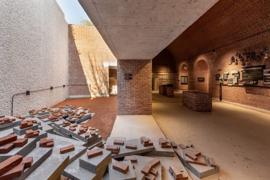 Art installation of scattered bricks in a museum courtyard leading into a brick exhibition hall.