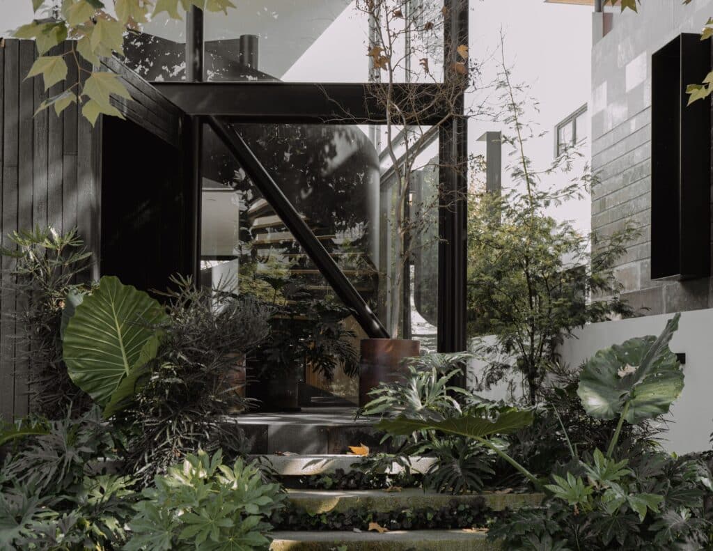 Casa EV residential design in Guadalajara featuring innovative integration of privacy, natural light, wooden materials, interconnected living spaces, central staircase, and landscaped exterior blending indoor and outdoor experiences.