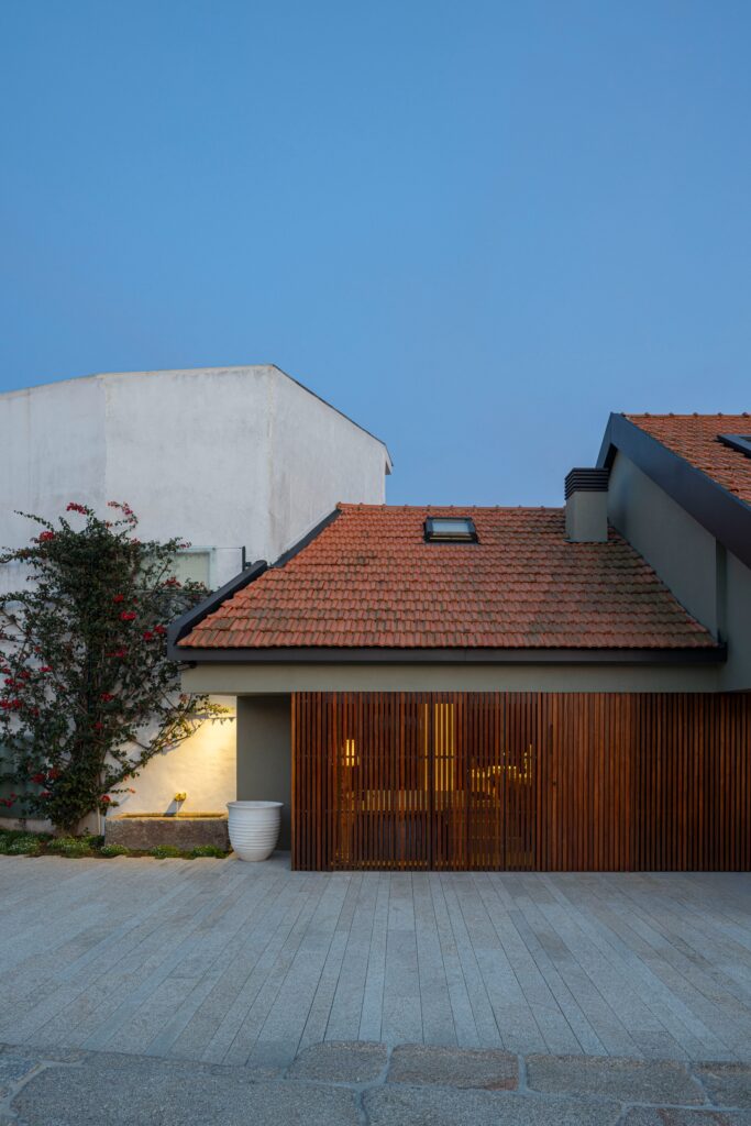 Night view of Casa do Engenho exterior with warm lighting shining through wooden louvers under a traditional tiled roof.