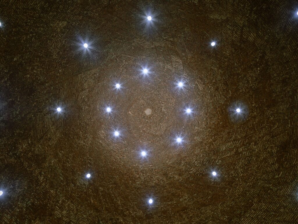 Looking up at the interior of a brick dome with a spiral pattern and integrated small lights.