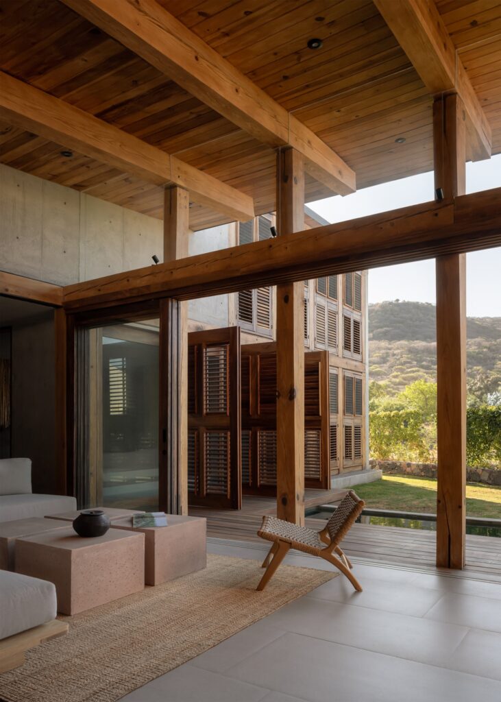 Interior of Queretaro House with large wooden shutters opening to a garden, featuring minimalist concrete furniture and natural textures.