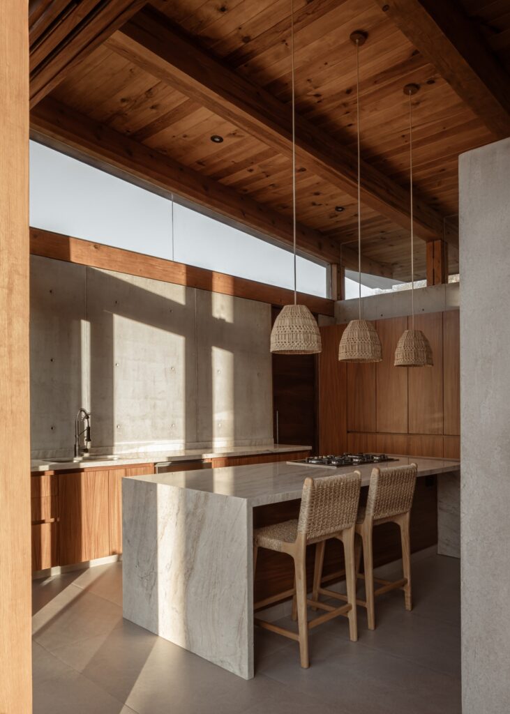 High-end kitchen in Queretaro House featuring a marble island, wooden cabinets, and woven pendant lights.