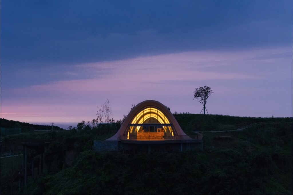 The illuminated arched interior of the Pujiang Platform at dusk, viewed from across the dark mountain slope.