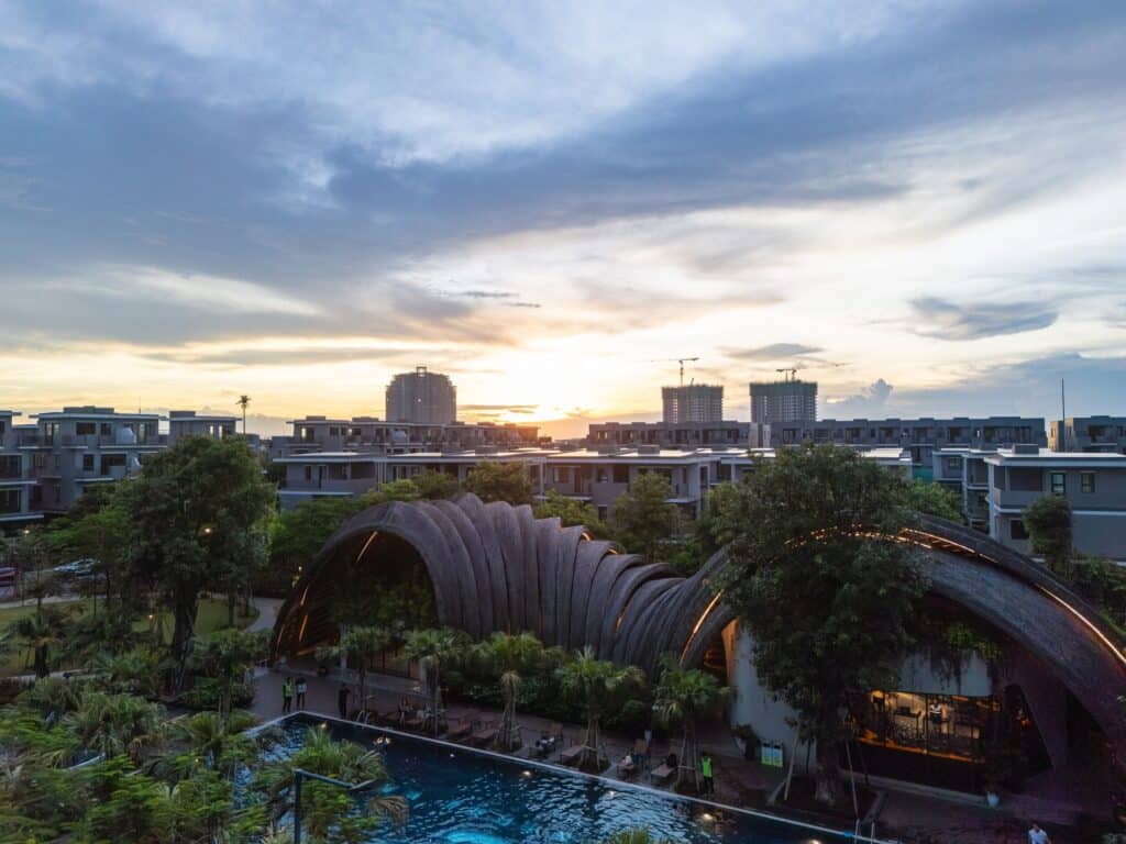 Wide-angle evening view of Goot Garden House with illuminated arched roofs reflecting in the swimming pool under a sunset sky.