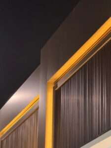 Modern architectural facade detail featuring dark vertical cladding slats illuminated by warm golden cove lighting.