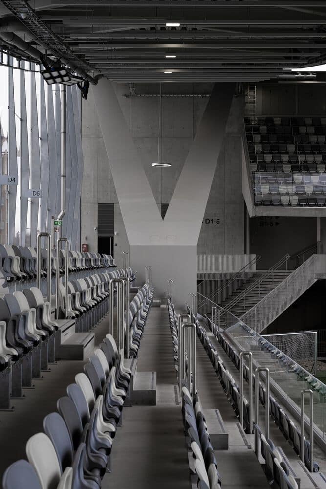Interior walkway and seating in a modern stadium with exposed concrete architecture and neutral-colored seats.