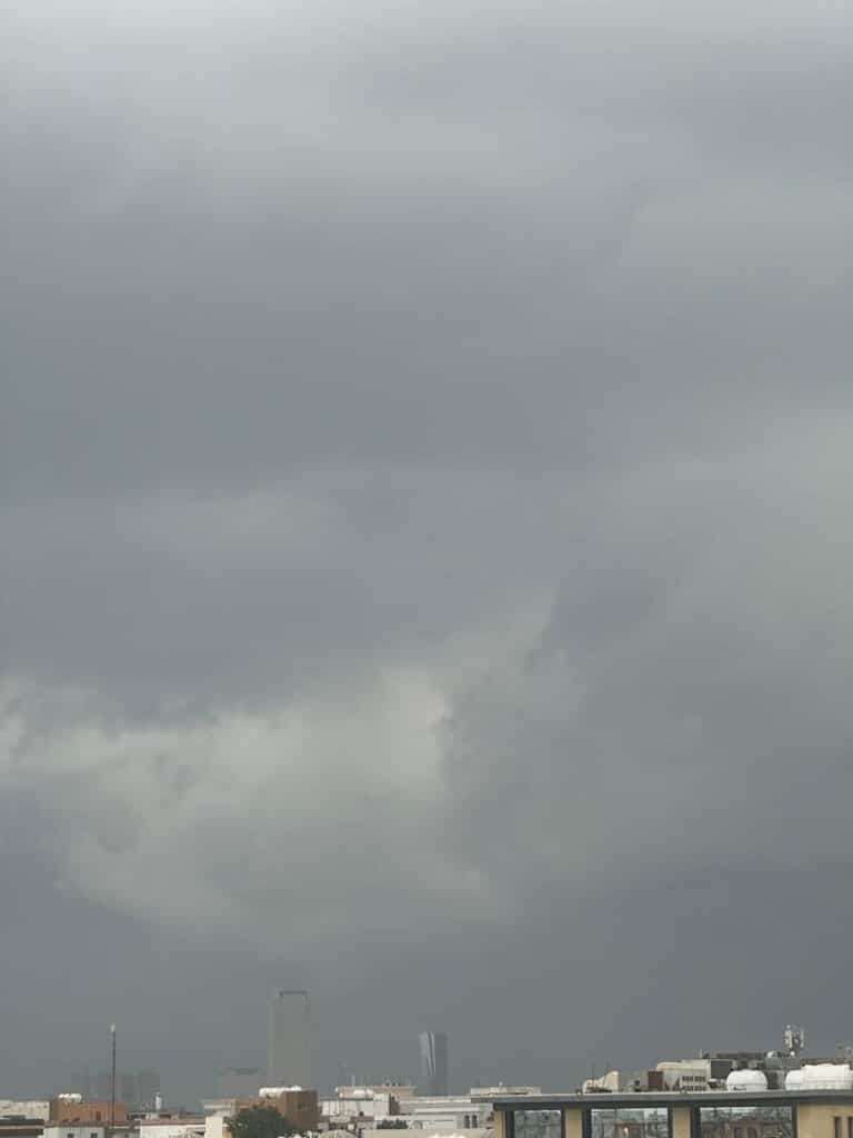 Dense gray nimbus clouds hovering over a city skyline, signaling an approaching heavy rainstorm.