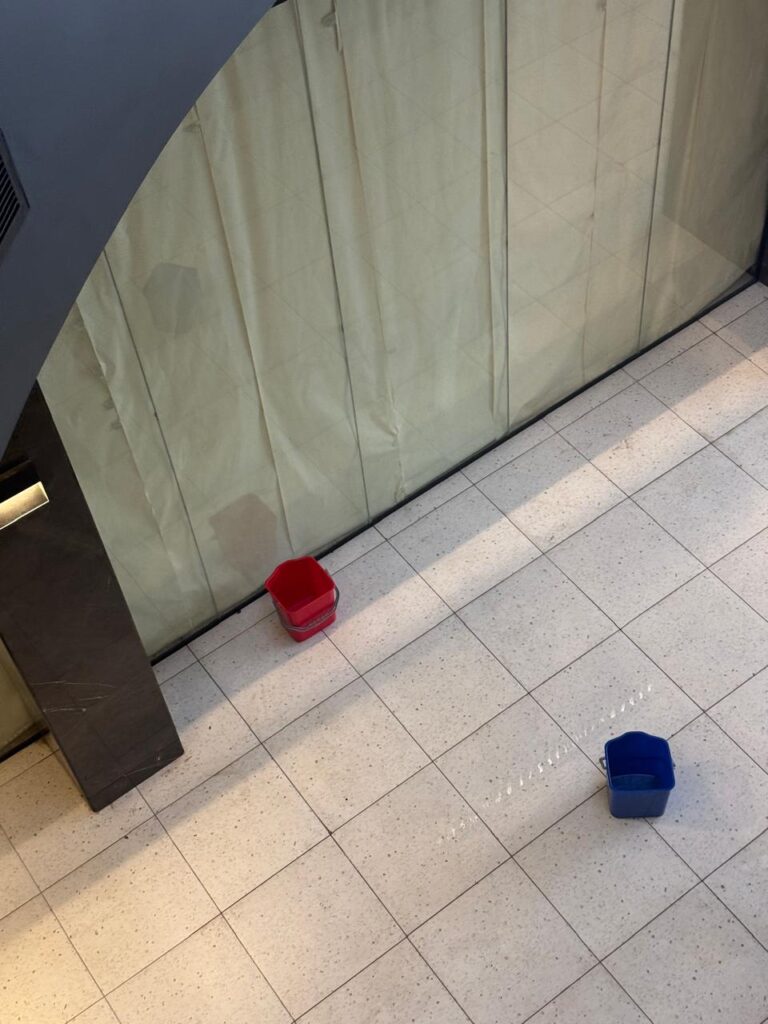 Plastic buckets placed on a modern lobby floor to collect rainwater leaking from the ceiling.