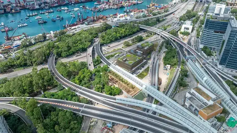 Aerial view of the Central Kowloon Bypass in Hong Kong, showing elevated roadways weaving through dense urban fabric and green corridors near the harbor.
