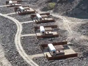 Aerial view of Nomad Kalba’s off-grid accommodation trailers nestled in rocky mountain terrain, each enclosed by low wooden fences and connected by winding dirt paths — environmental reuse applied to hospitality infrastructure.
