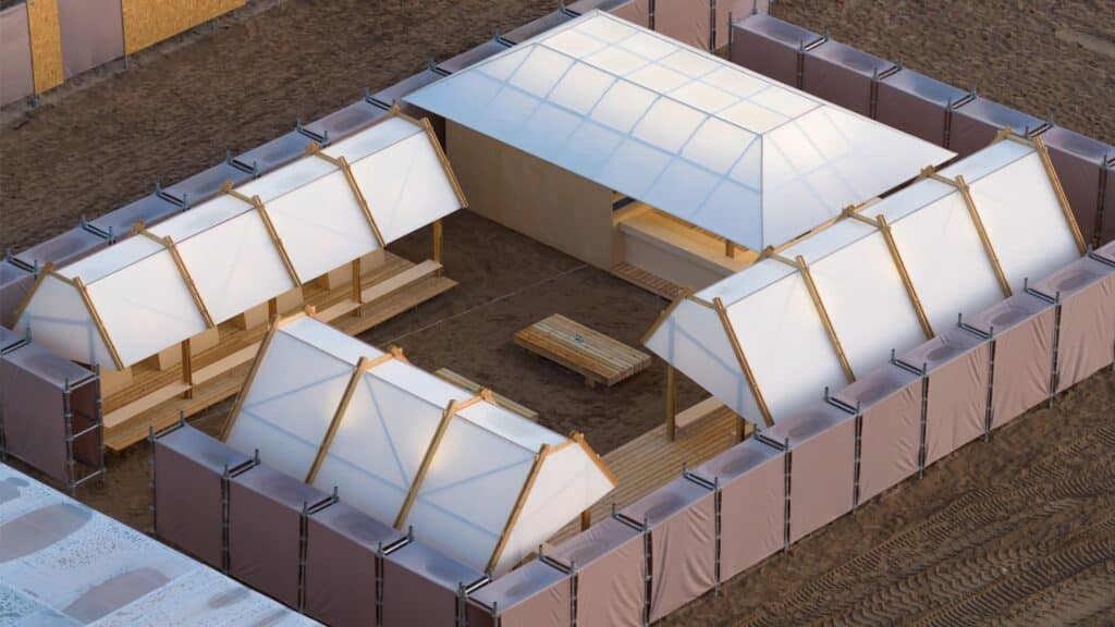 Aerial view of a large-scale temporary installation under construction on a beach at dusk, featuring modular structures and illuminated pavilions  exemplifying ephemeral architecture.