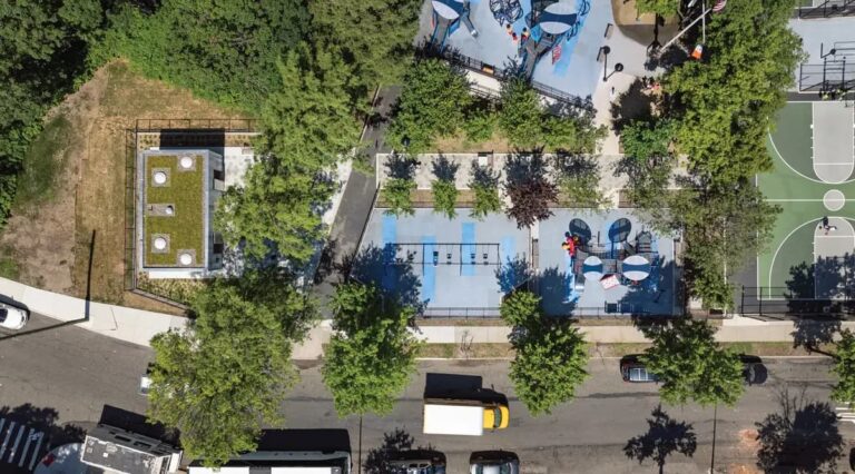 Aerial view of the award-winning Staten Island public restroom at Lopez Playground, featuring a green roof and modular design integrated into the urban park landscape with adjacent playground and basketball court.