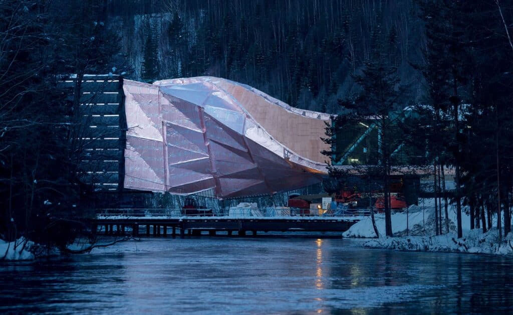Architectural sustainability in practice  The Twist building at Kistefos Museum, Norway, wrapped in protective film during winter construction, nestled between forest and river.