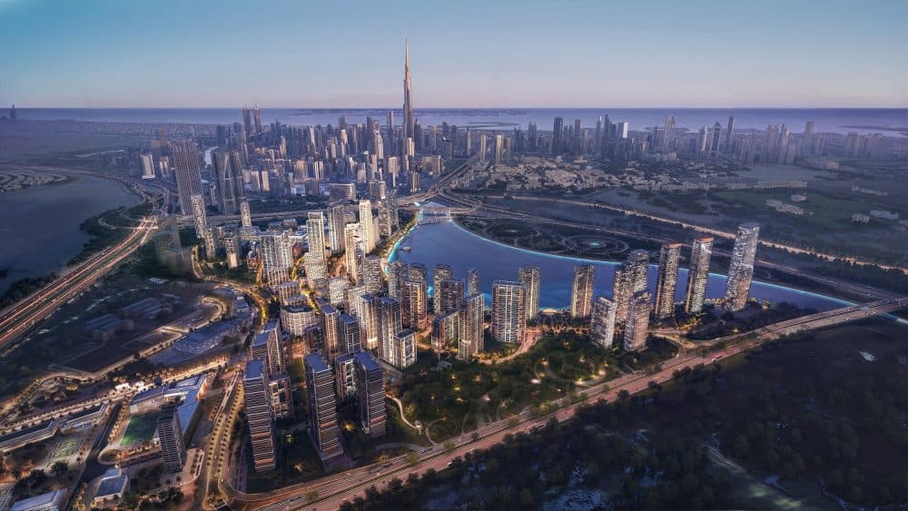 Aerial view of Dubai Design District’s expanded residential masterplan at dusk, showing high-rise towers along a waterfront canal with Burj Khalifa in the background.