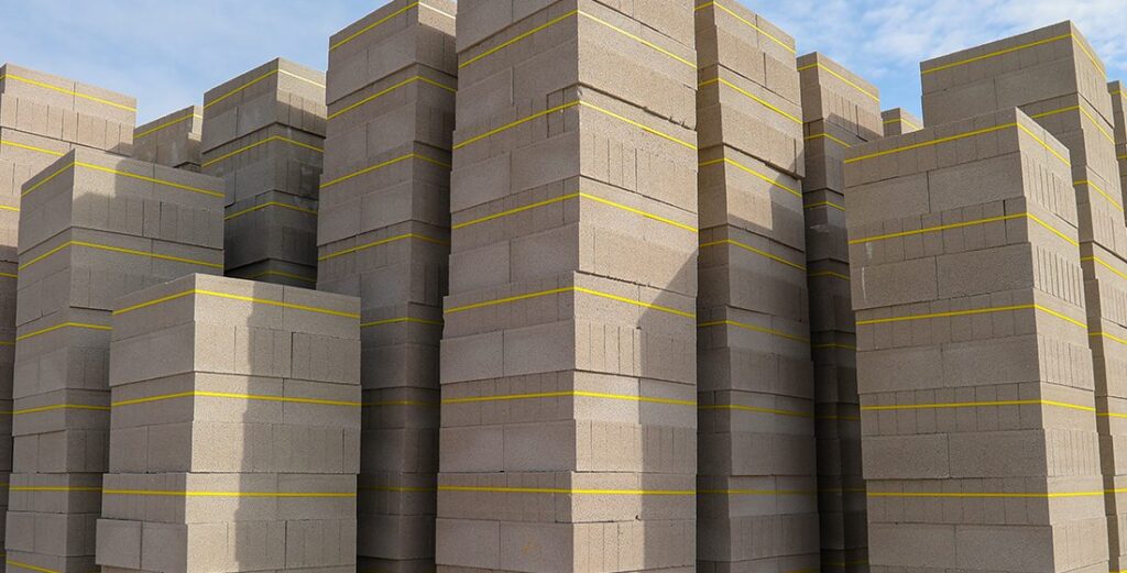 أكوام من وحدات الطوب الخرساني مربوطة بشرائط صفراء تحت سماء صافية  مادة بناء قياسية لتطبيقات هيكلية وغير هيكلية.