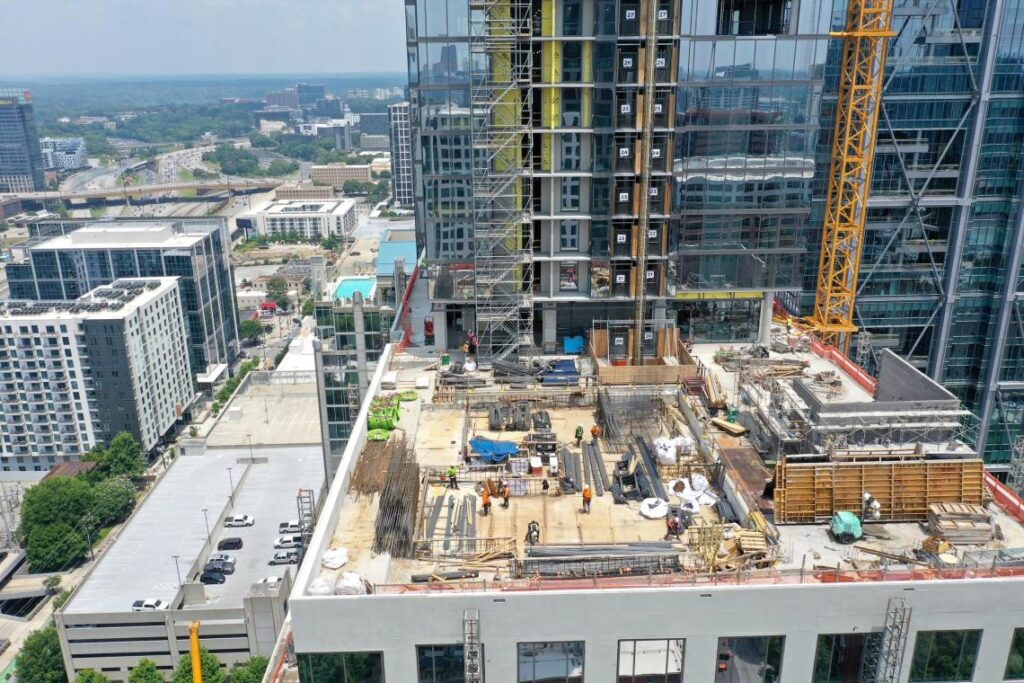 Atlanta mixed-use tower under construction, showing exposed steel and concrete framework with workers on the rooftop against Midtown&rsquo;s high-rise backdrop.