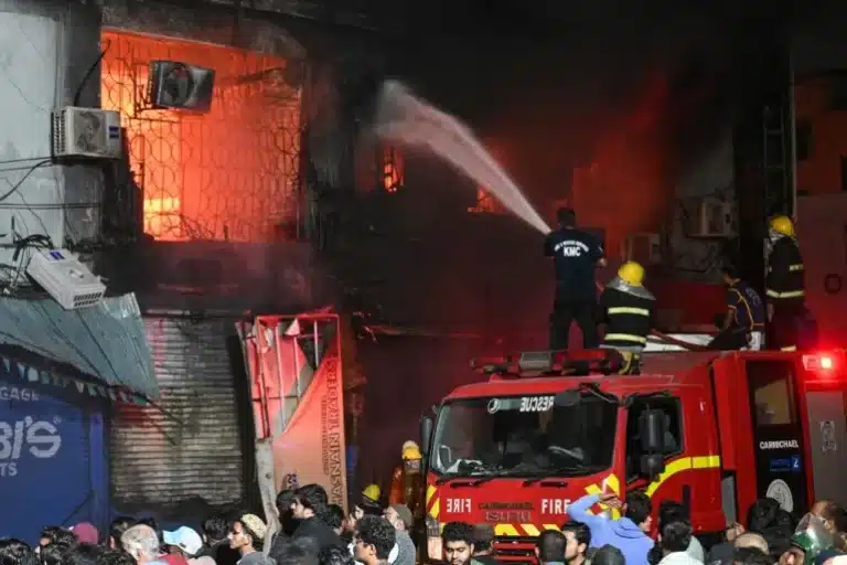 Firefighters battle intense flames engulfing a multi-storey commercial building in downtown Karachi during the January 18, 2026 urban shopping center fire, as crowds observe from street level.