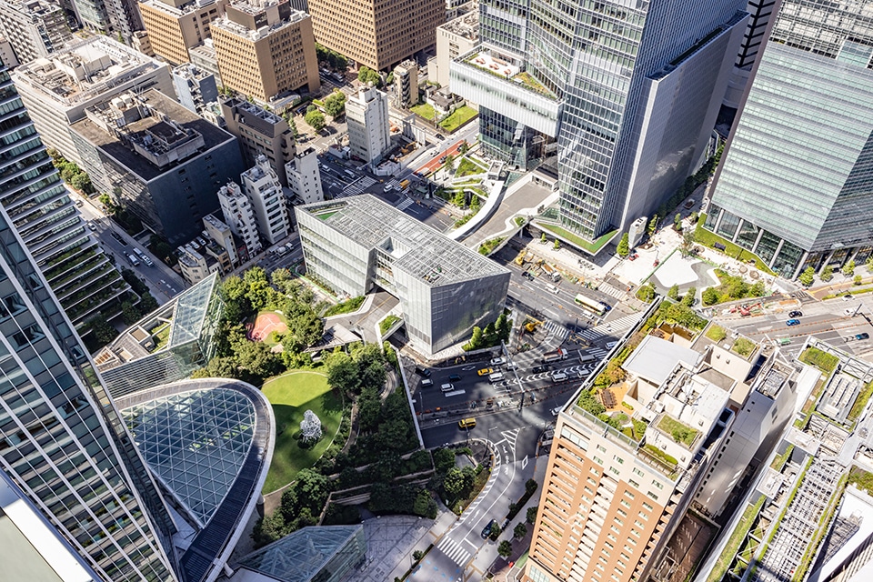 Aerial view of a Tokyo Transit-Oriented Development integrating glass towers, green rooftops, and pedestrian pathways into a dense urban fabric.