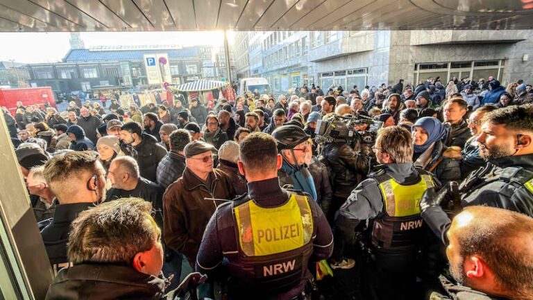 Crowd of onlookers and journalists surrounding police officers at the scene of a bank vault security breach in Gelsenkirchen, Germany.
