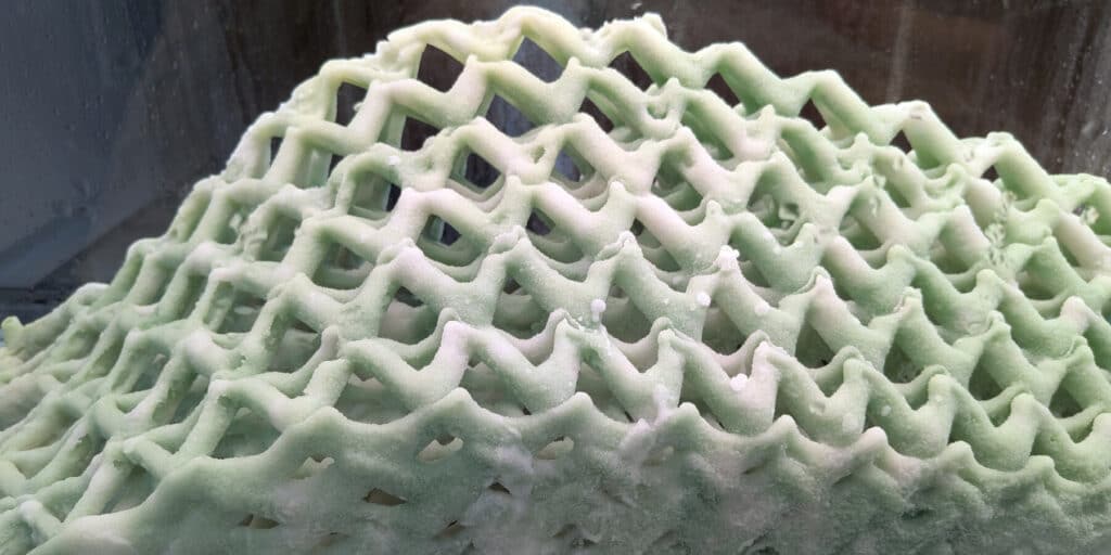 Close-up of 3D-printed bio-integrated facade lattice from Living Building prototype, showing microorganism-activated surface texture and carbon-mineral deposition.